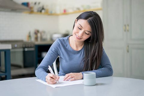 Casual Latin American woman at home writing on documents like bills or letters